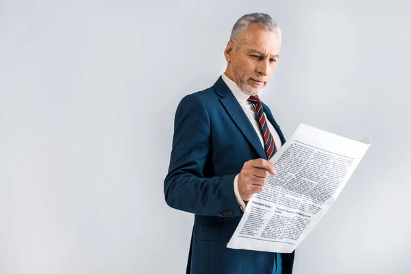 Mature businessman reading newspaper while standing isolated on grey — Stock Photo