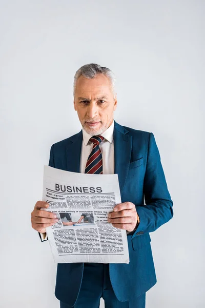 Mature man in formal wear holding business newspaper while standing isolated on grey — Stock Photo