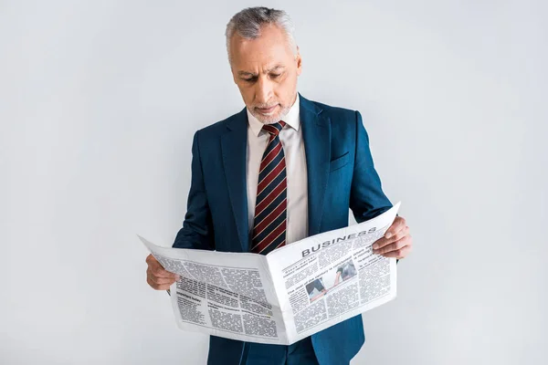 Hombre maduro en traje leyendo periódico de negocios mientras está de pie aislado en gris - foto de stock