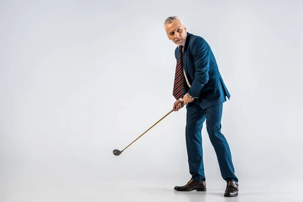 Mature businessman holding golf club while playing on grey — Stock Photo