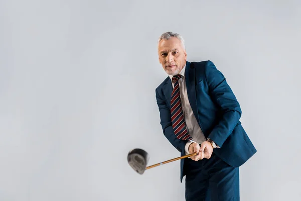 Selektiver Fokus eines gut gelaunten, reifen Geschäftsmannes, der einen Golfschläger hält, während er isoliert auf grau spielt — Stockfoto