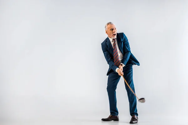 Surpreendido homem de negócios maduro segurando clube de golfe enquanto joga em cinza — Fotografia de Stock