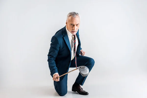 Confident mature man in suit holding golf club and while sitting on grey — Stock Photo