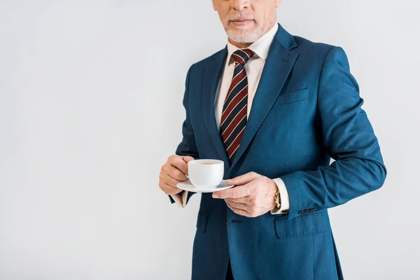 Abgeschnittene Ansicht eines gestandenen Geschäftsmannes in formeller Kleidung mit Untertasse und Tasse isoliert auf grau — Stockfoto