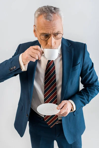 Vue aérienne d'un homme d'affaires mature tenant une soucoupe et buvant du café à partir d'une tasse isolée sur gris — Photo de stock