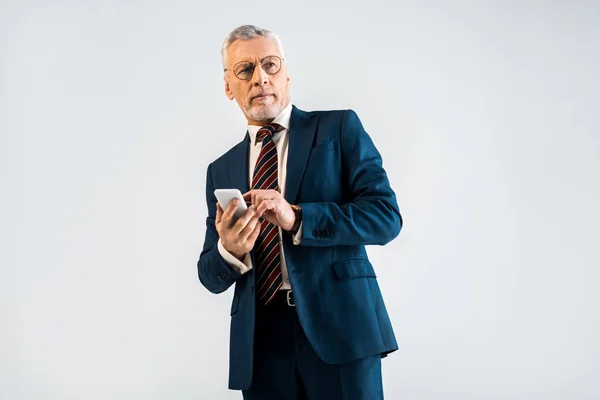 Reifer Geschäftsmann im Anzug hält Smartphone isoliert auf grau — Stockfoto