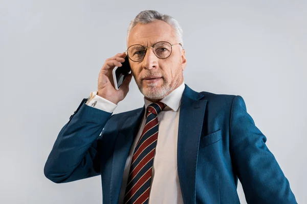 Зрелый бизнесмен в костюме разговаривает на смартфоне изолирован на серый — стоковое фото