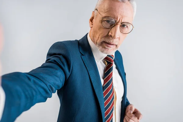 Mature homme d'affaires en costume prendre selfie et regarder caméra isolé sur gris — Photo de stock