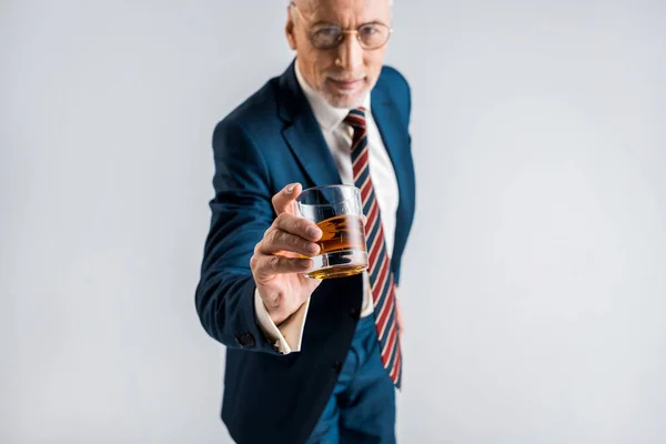 Selektiver Fokus des Glases mit Whiskey in der Hand eines reifen Geschäftsmannes isoliert auf grau — Stockfoto