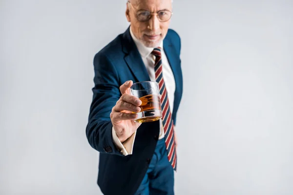 Selective focus of glass with whiskey in hand of mature businessman isolated on grey — Stock Photo