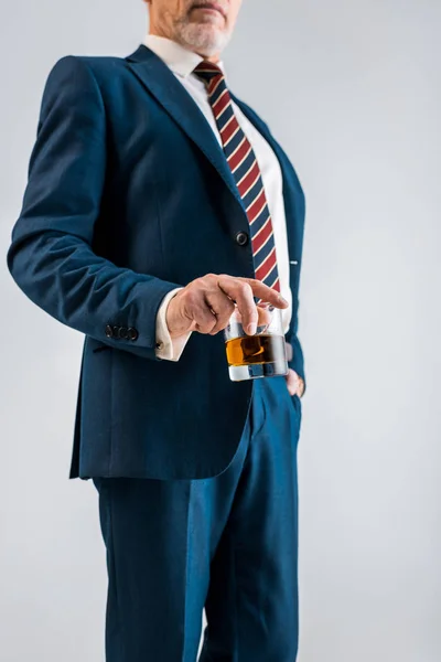 Selektiver Fokus eines gestandenen Geschäftsmannes im Anzug, der Glas mit Whiskey auf Grau isoliert hält — Stockfoto