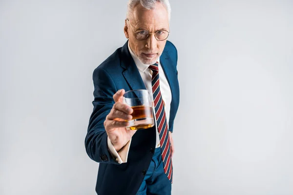 Enfoque selectivo de hombre de negocios maduro en el desgaste formal celebración de vidrio con whisky aislado en gris - foto de stock