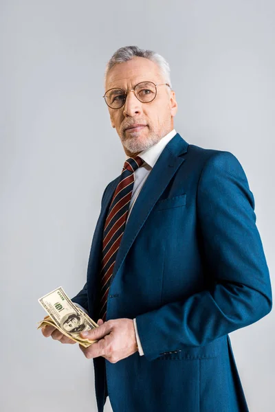 Schöner reifer Geschäftsmann mit Brille und formeller Kleidung, der Dollarnoten isoliert auf grau hält — Stockfoto