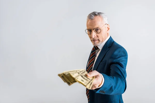 Selective focus of mature man in glasses and formal wear holding dollar banknotes isolated on grey — Stock Photo