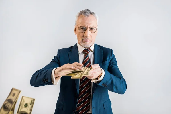 Foco seletivo do empresário maduro em óculos e desgaste formal jogando em notas de dólar de ar isolado em cinza — Fotografia de Stock