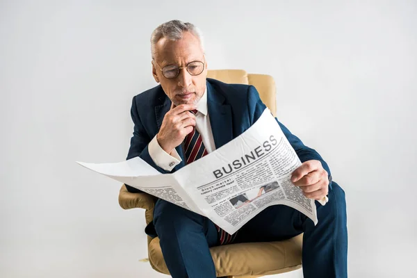 Homme d'affaires mature assis dans le fauteuil et la lecture journal d'affaires isolé sur gris — Photo de stock