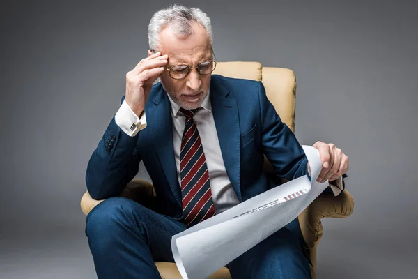 Stanco uomo d'affari maturo in tuta tenere cartello mentre seduto in poltrona su grigio — Foto stock