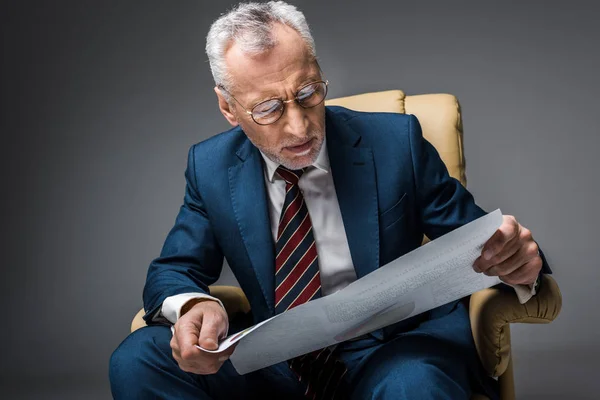 Hombre de negocios maduro en traje mirando la pancarta mientras está sentado en un sillón en gris - foto de stock