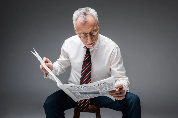 Reifer Geschäftsmann im Anzug liest Reisezeitung auf grau — Stockfoto