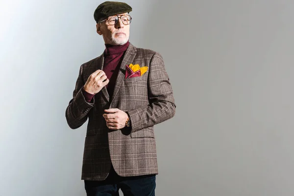 Elegante uomo di mezza età in occhiali e cappuccio in piedi sul grigio — Foto stock