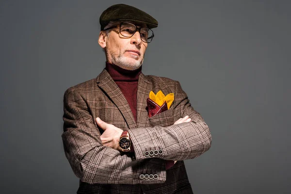 Stilvoller Mann mittleren Alters mit Brille und Mütze steht mit verschränkten Armen auf grau — Stockfoto