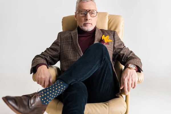 Middle aged man in glasses sitting in armchair with crossed legs isolated on grey — Stock Photo