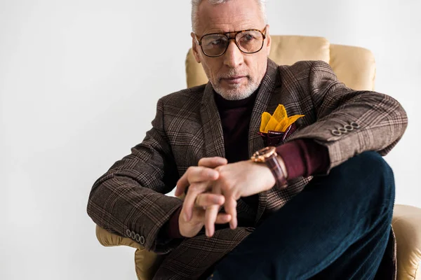 Selektiver Fokus eines Mannes mittleren Alters mit Brille, der in einem Sessel sitzt, isoliert auf grau — Stockfoto