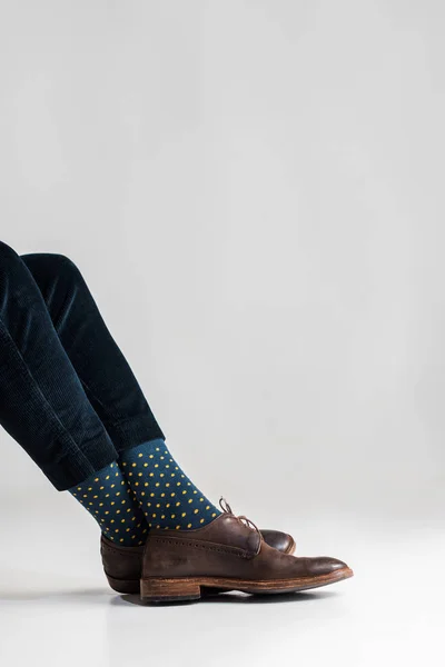 Обрезанный вид человека со скрещенными ногами на сером — стоковое фото