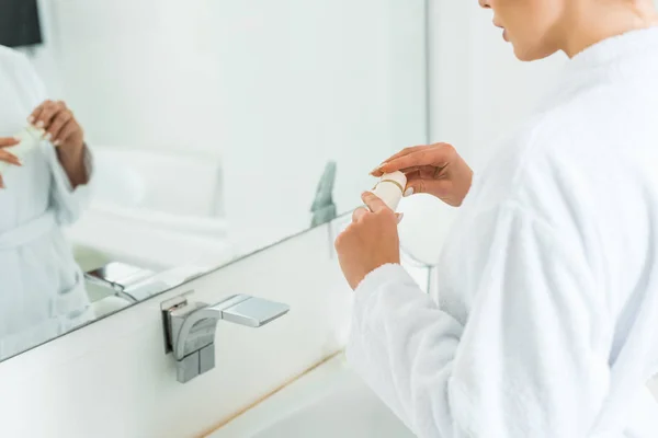 Vista recortada de la mujer en el tubo de apertura de albornoz con pasta de dientes en el baño - foto de stock