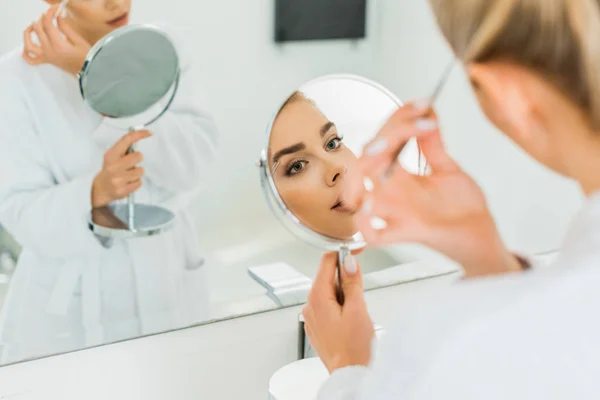 Foyer sélectif de belle femme plumant les sourcils avec une pince à épiler dans la salle de bain — Photo de stock