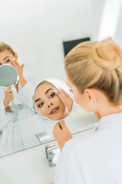 Foco seletivo da bela mulher tocando o rosto e olhando para o espelho no banheiro — Fotografia de Stock