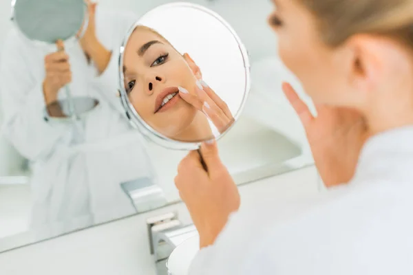 Selective focus of woman touching face and looking at mirror in bathroom — Stock Photo