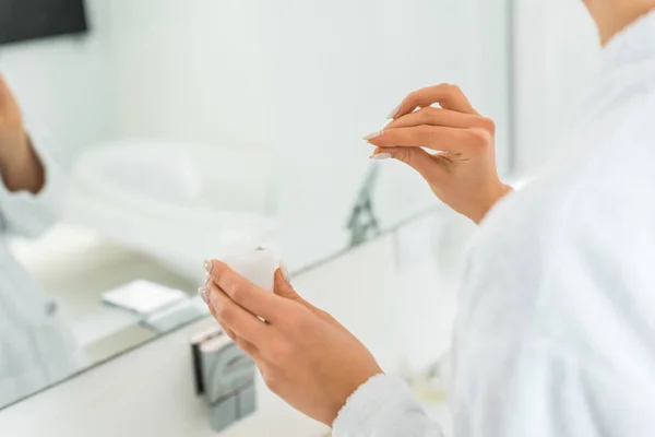 Selective focus of young adult woman holding cosmetic cream in bathroom — Stock Photo