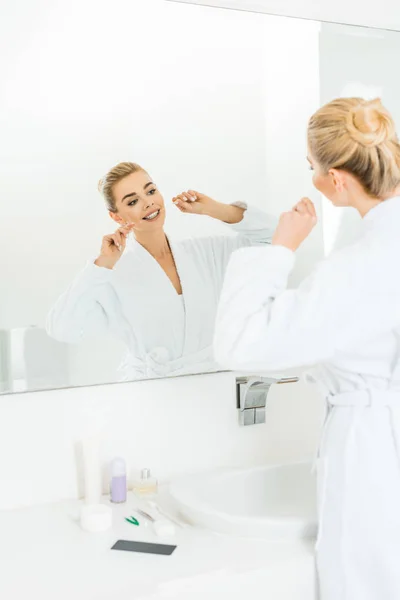 Selective focus of beautiful and blonde woman in white bathrobe brushing teeth with dental floss — Stock Photo