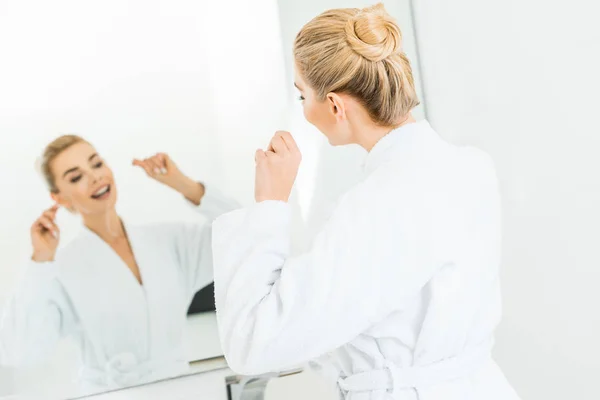 Messa a fuoco selettiva di bella e bionda donna in accappatoio bianco lavarsi i denti con filo interdentale — Foto stock