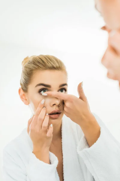 Selective focus of attractive and blonde woman in white bathrobe attaching contact lens — Stock Photo