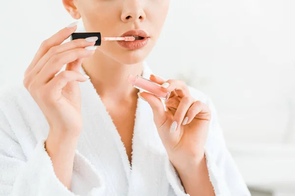 Vista recortada de la mujer en albornoz blanco aplicando brillo de labios en el baño — Stock Photo