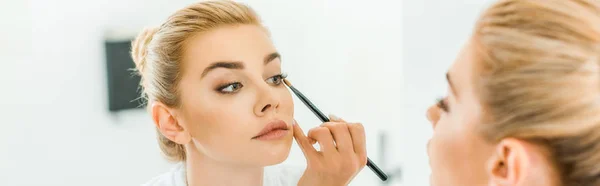 Panoramaaufnahme einer blonden und schönen Frau, die Lidschatten mit Kosmetikpinsel aufträgt — Stockfoto