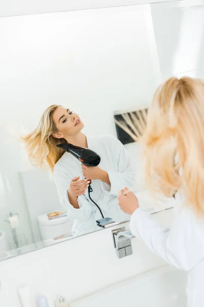 Selective focus of beautiful and blonde woman in white bathrobe drying hair in bathroom — Stock Photo
