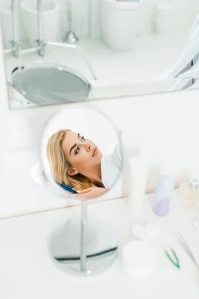 Selective focus of beautiful and blonde woman holding comb and looking away in bathroom — Stock Photo