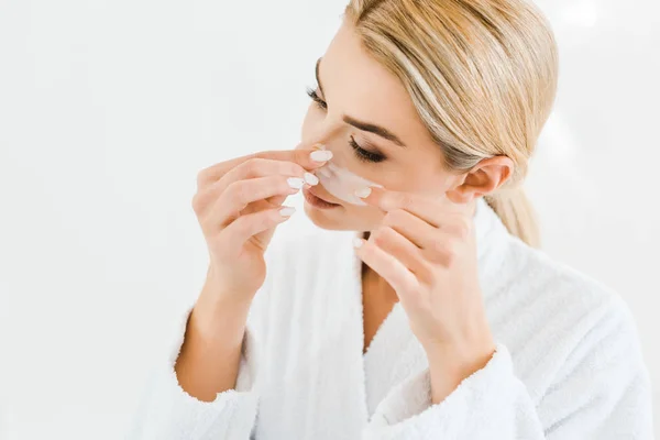 Blonde and attractive woman in white bathrobe applying eye patches in bathroom — Stock Photo