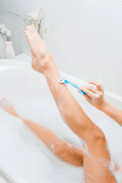 Vista parcial de la mujer tomando baño y afeitarse la pierna con afeitadora en el baño - foto de stock