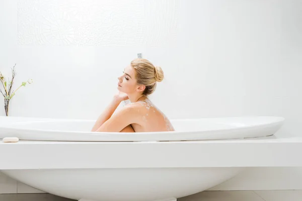 Vista lateral de mujer hermosa y rubia tomando baño con espuma en el baño - foto de stock