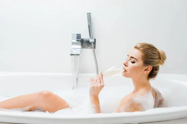 Attraktive Frau badet und trinkt Getränke aus Champagnerglas im Badezimmer — Stockfoto