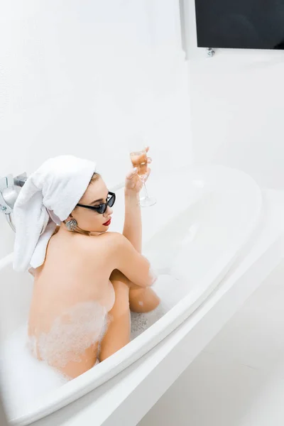 Rückansicht der schönen Frau mit weißem Handtuch und Sonnenbrille, die baden und Champagnerglas in der Hand hält — Stockfoto