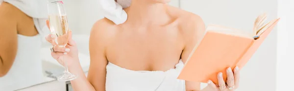 Panoramic shot of woman in towel holding champagne glass reading book in bathroom — Stock Photo