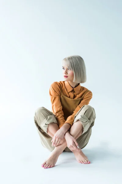 Schöne stylische junge Frau sitzt mit überkreuzten Beinen auf weiß — Stockfoto