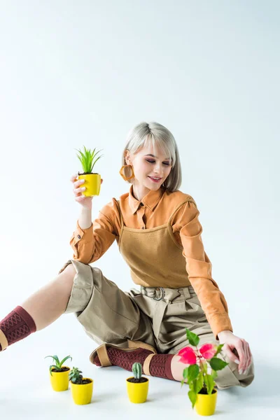 Bela menina elegante sentado com vasos de flores e sorrindo no branco — Fotografia de Stock