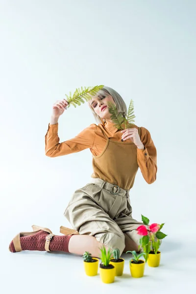 Belle fille élégante posant avec des feuilles de fougère près de pots de fleurs sur blanc — Photo de stock