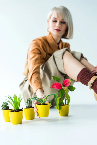 Selective focus of flower transplants with beautiful stylish girl sitting on white — Stock Photo
